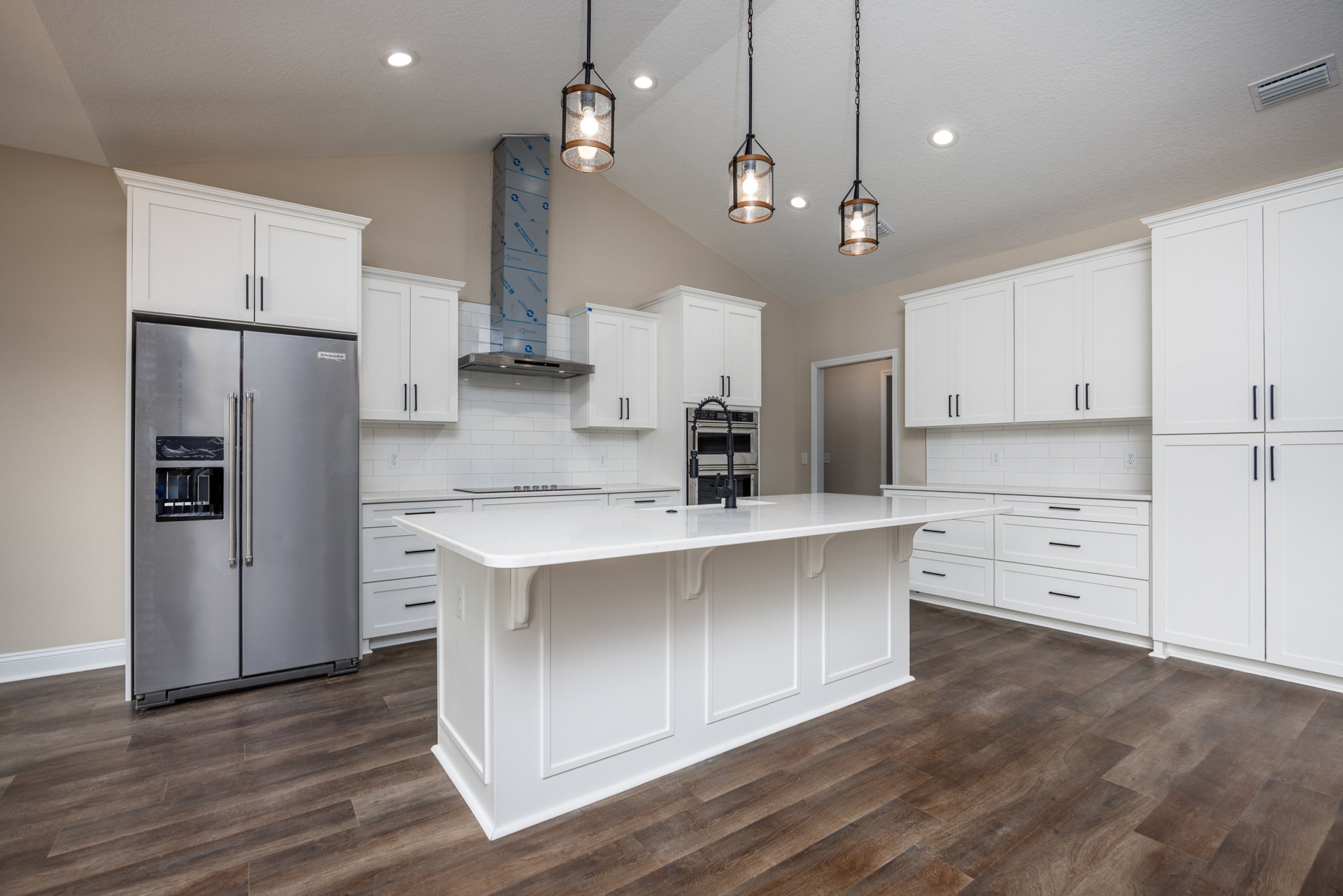 White kitchen with shaker cabinets, spacious island featuring a black faucet, stainless steel refrigerator, light wood flooring, and pendant light with glass shade
