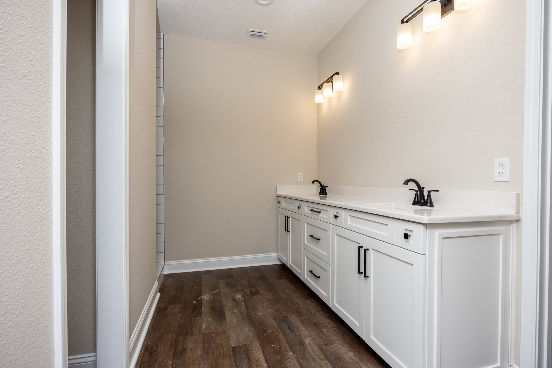 Bathroom with white shaker cabinets, matte black faucets and handles, white tile backsplash, and a three-light fixture above the sink
