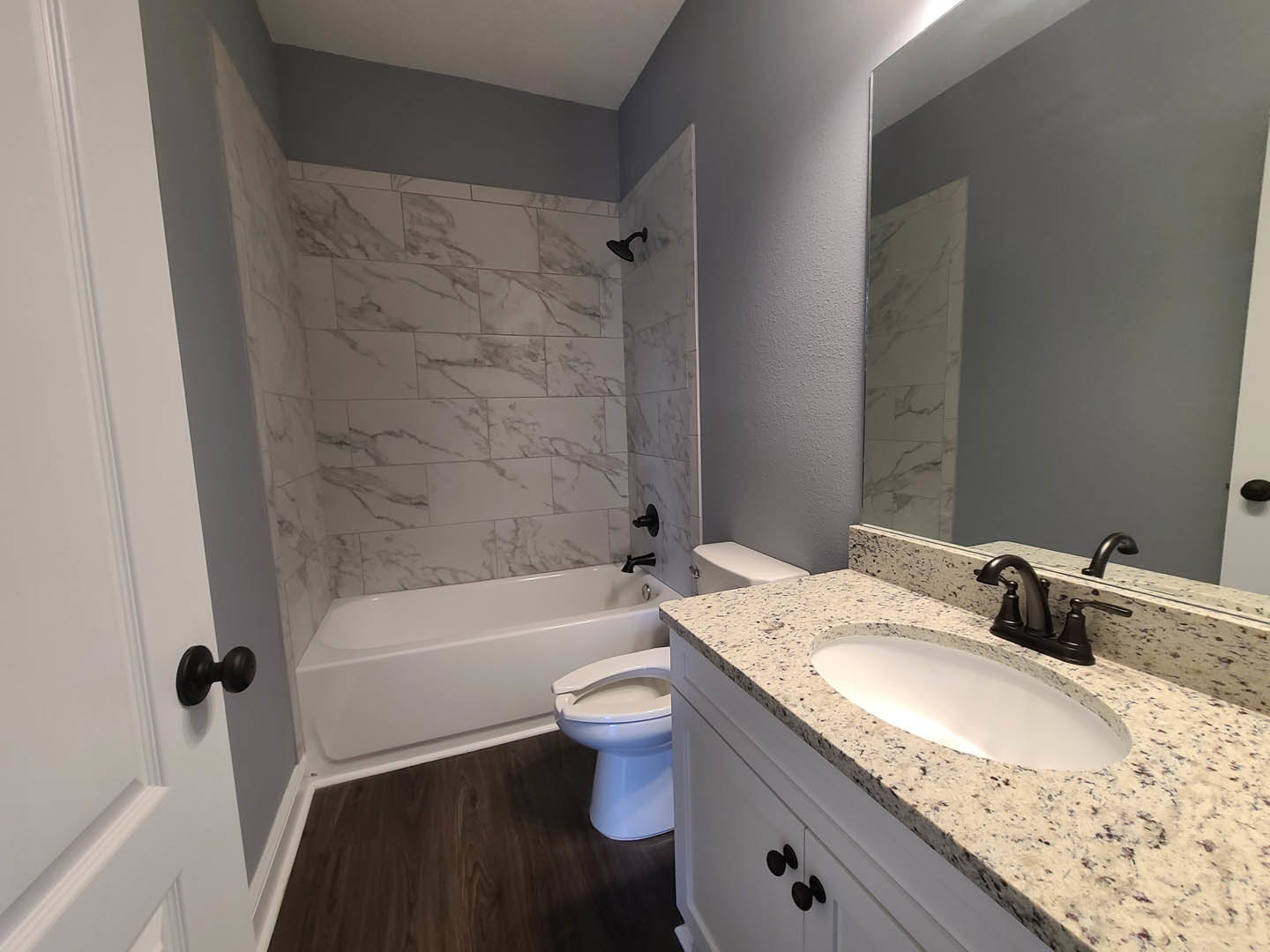 Marble countertop with undermount sink, matte black faucet, white cabinetry, and black hardware in a modern bathroom