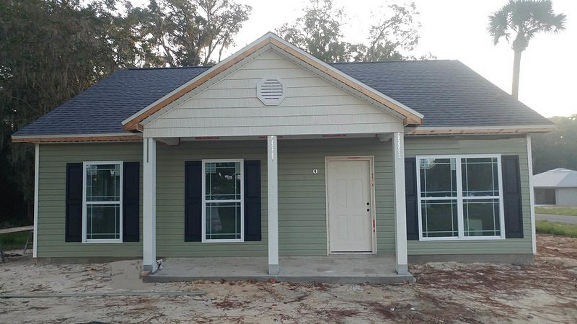Front porch with white siding, white door featuring four black knobs, black-framed window, roof vent, and tree in background