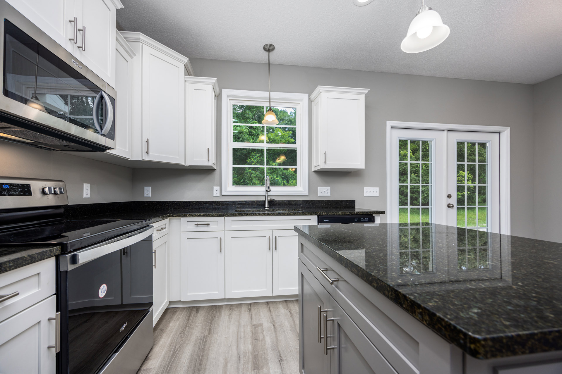 White kitchen cabinets with silver handles, black granite countertops, stainless steel microwave, ceiling light fixture, window providing natural light, and built-in sink.