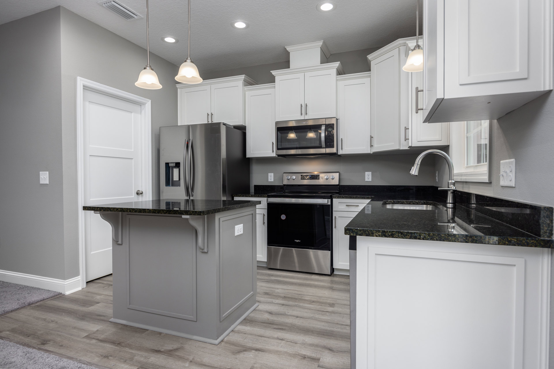 White kitchen cabinets with black countertops, stainless steel microwave and stove, green-lit pole, silver ceiling pole, and close-up of a light switch