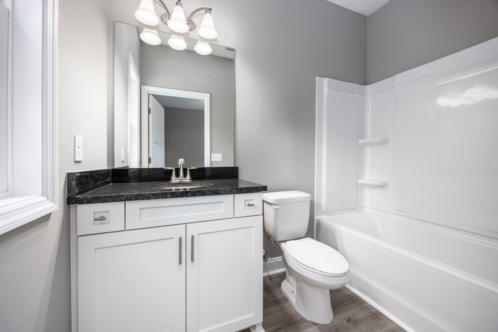 Bathroom with white bathtub, white toilet, wall-mounted sink, open door reflecting in large mirror, tile flooring, and cluster of pendant light fixtures.