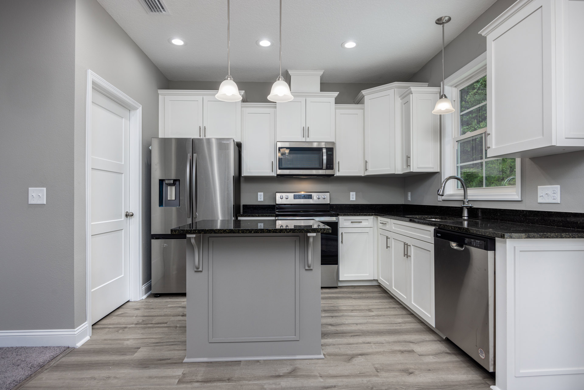 White kitchen with black countertops, white cabinets, kitchen island with black surface, built-in microwave containing a glass of liquid, light switch on wall, close-up of metal