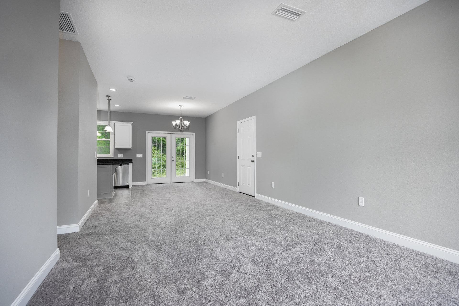 Grey carpeted floor, white walls, white door with silver knobs, double glass-paneled doors, window overlooking trees, smooth plaster ceiling