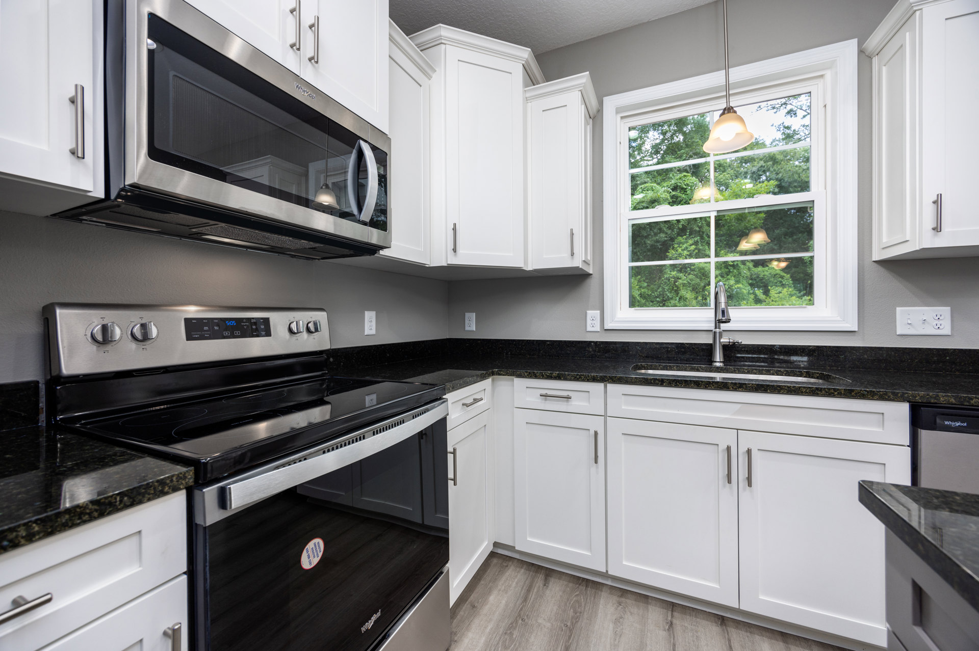 White kitchen cabinets with black appliances, including a gas stove and microwave, light streaming through a window, and countertops with a close-up of a white sticker featuring