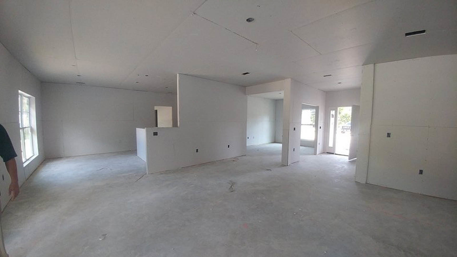 White-walled room with a single door, window allowing natural light, smooth plaster ceiling, and light-colored flooring