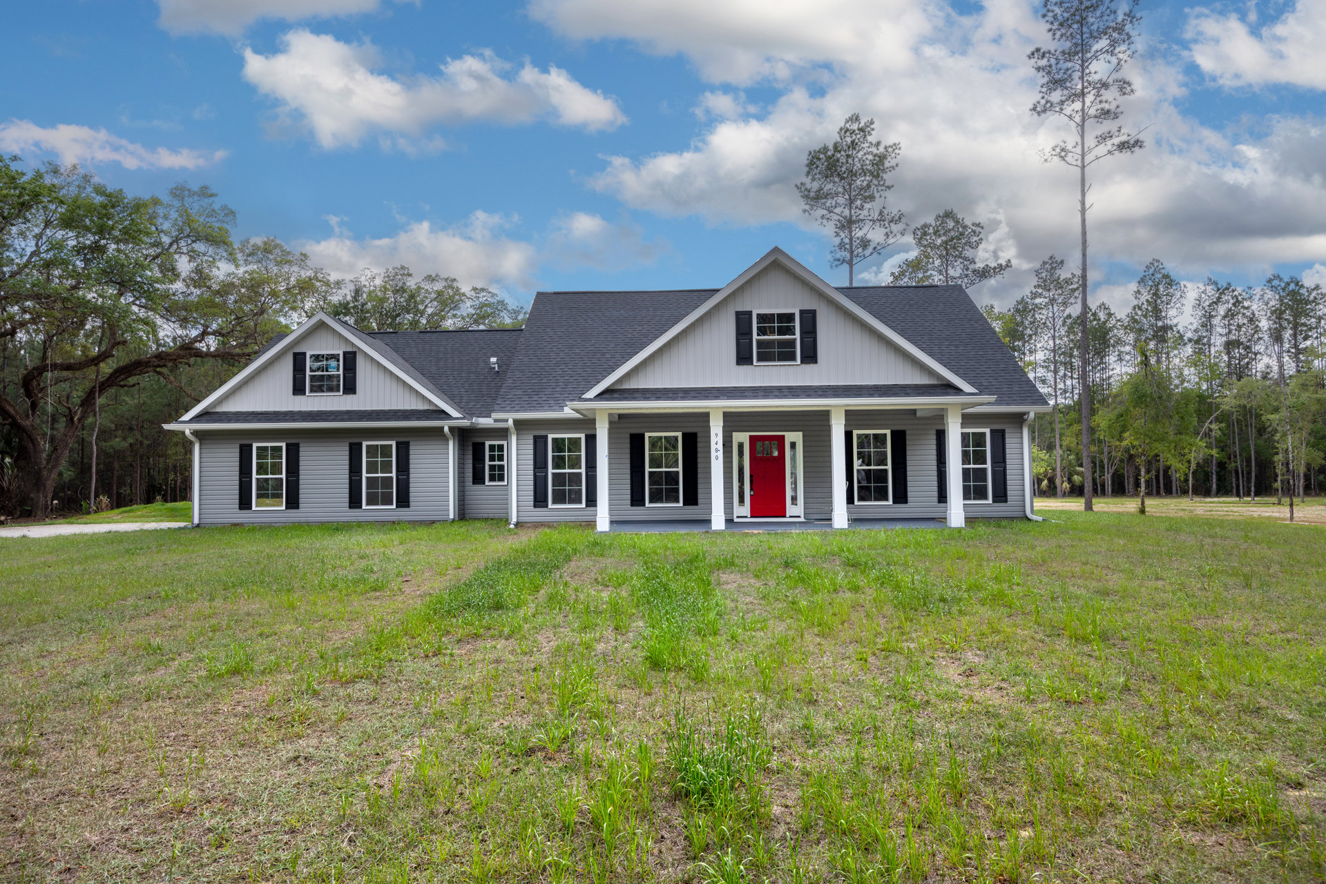 Two-story house with grey roof, red front door framed in white, white-trimmed windows, grassy lawn, and tall tree in front yard