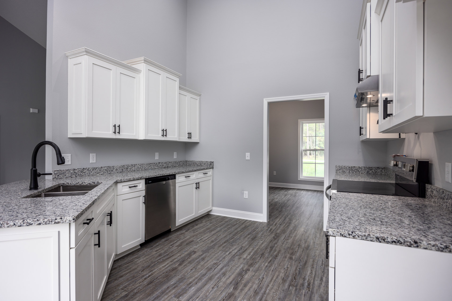 Granite countertops with white cabinets, black refrigerator and faucet, window overlooking trees, close-up of countertop, light-colored flooring