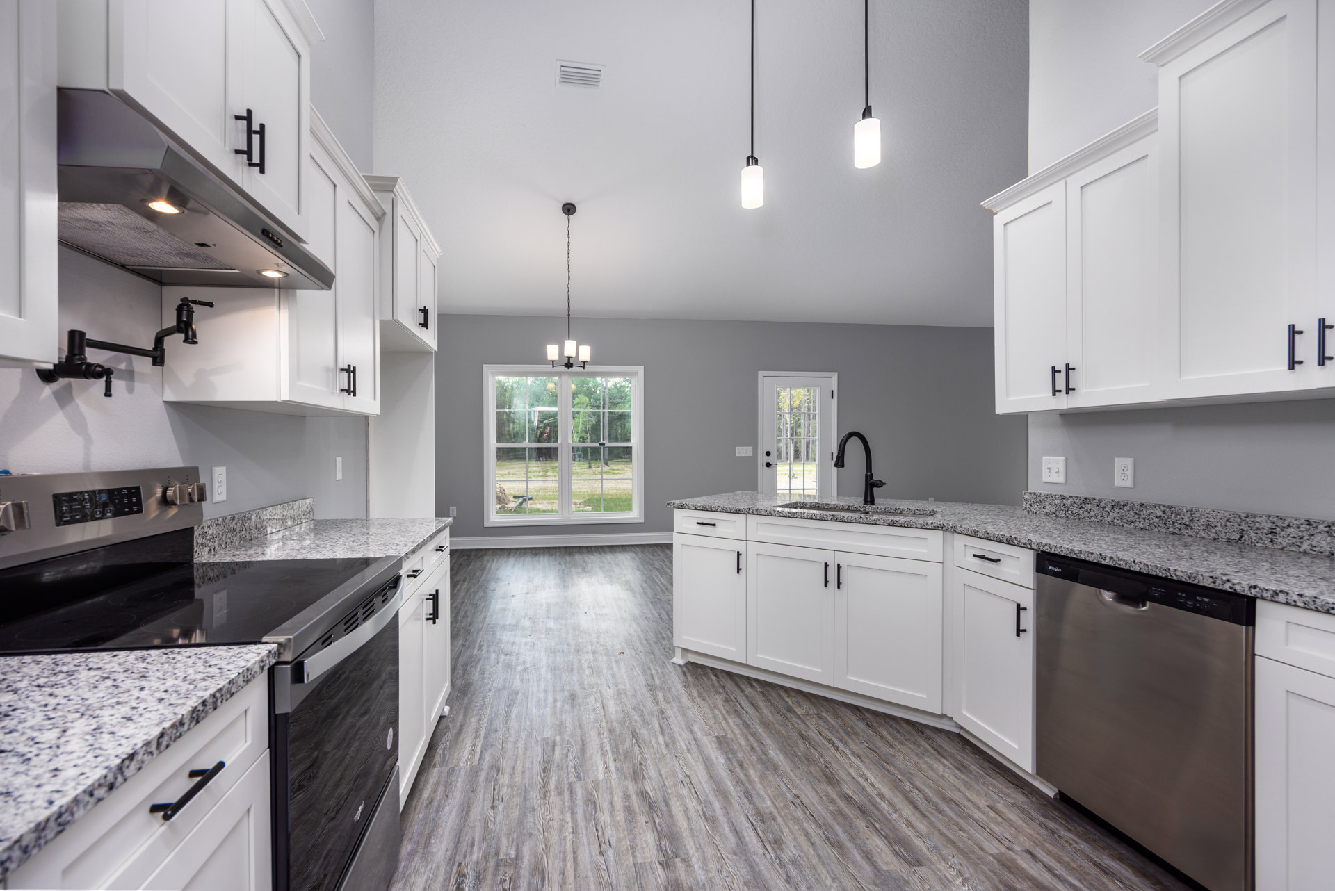 Kitchen with white cabinets, black appliances, granite countertops, stainless steel hood, dishwasher with handle, window overlooking yard, and white door with glass panel