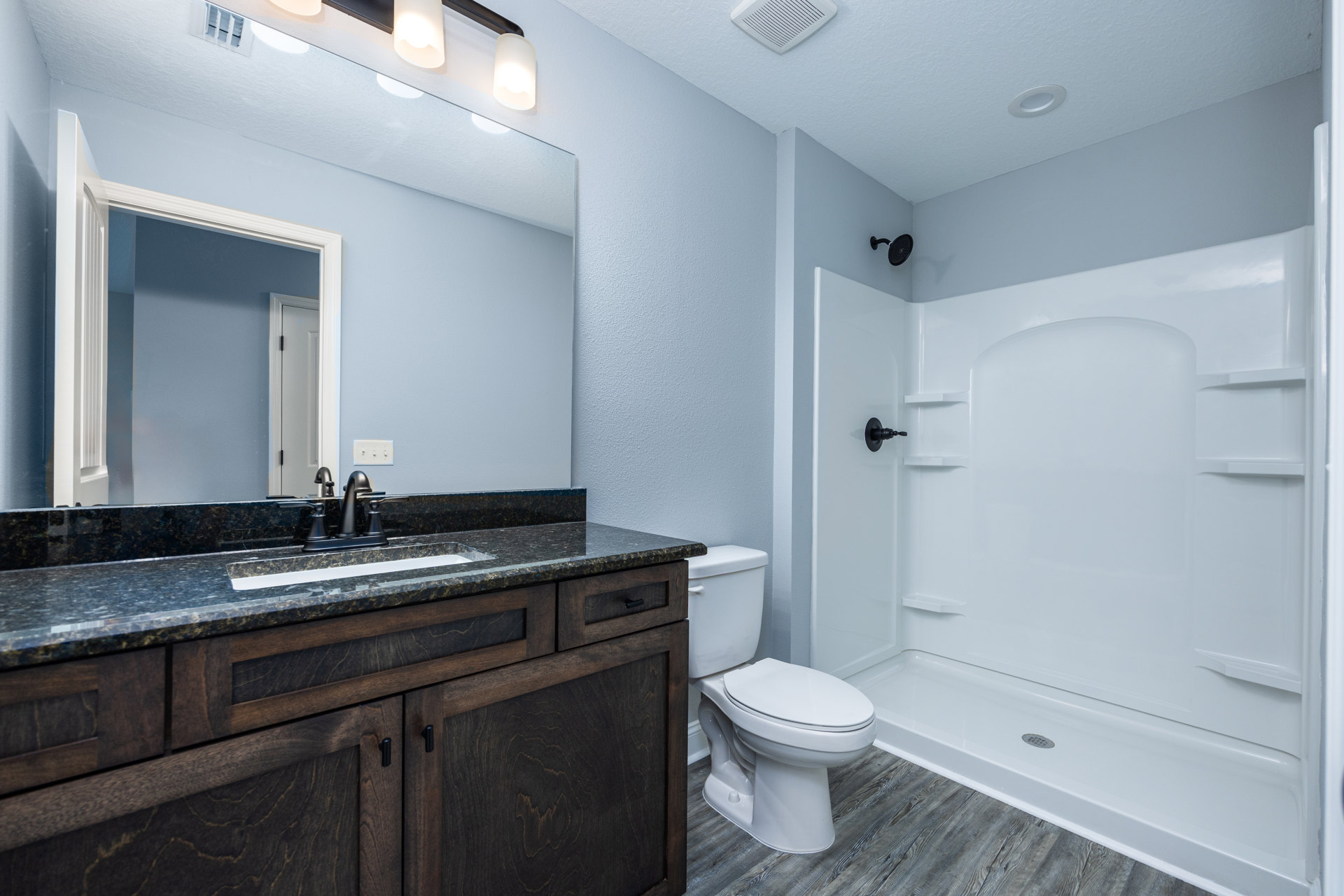 Modern bathroom featuring a white sink with chrome faucet, glass-enclosed shower with built-in shelves, white toilet, black wall switch, white ceiling vent, and recessed lighting.