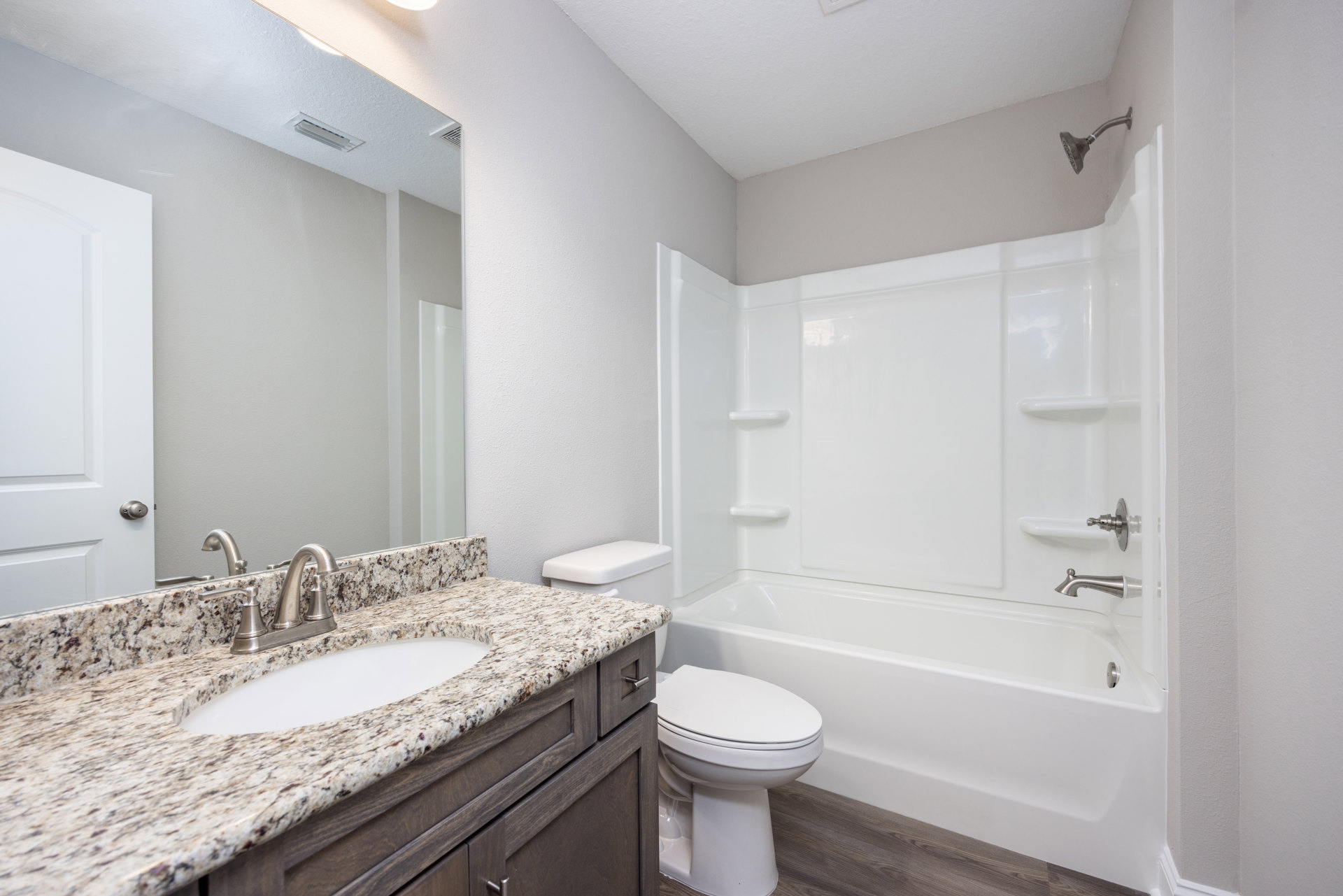 Marble countertop with undermount sink, chrome faucet, white toilet, tiled shower wall with showerhead, white painted walls