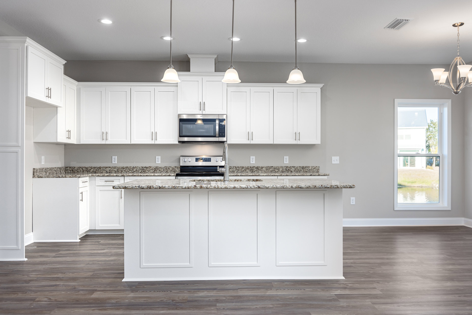 Kitchen featuring white cabinetry, granite countertops, central island, stainless steel microwave with illuminated window, white-framed window, ceiling light, and bell-shaped
