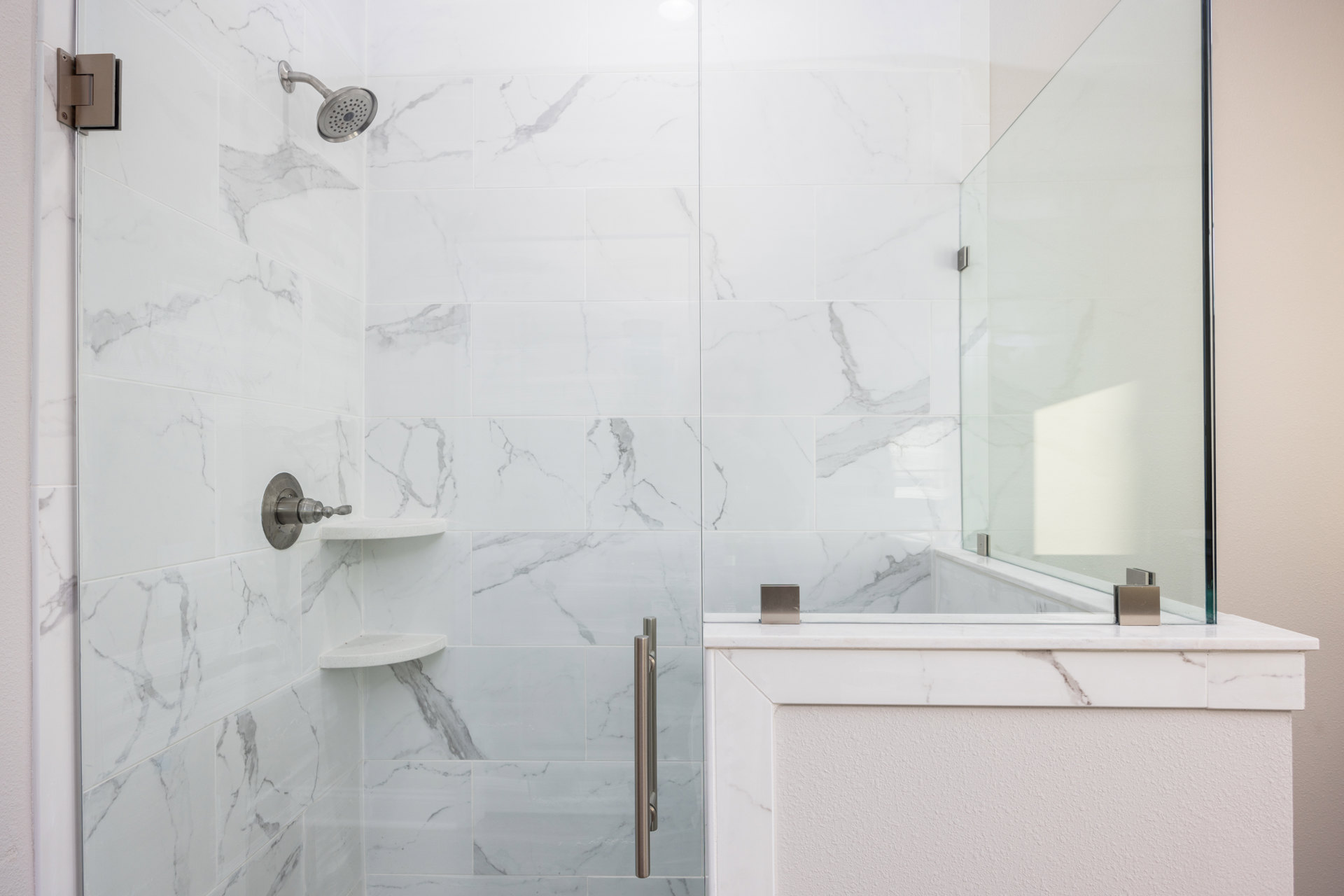 Walk-in shower with clear glass door, chrome shower head and faucet, white walls accented by marble trim, marble tile flooring