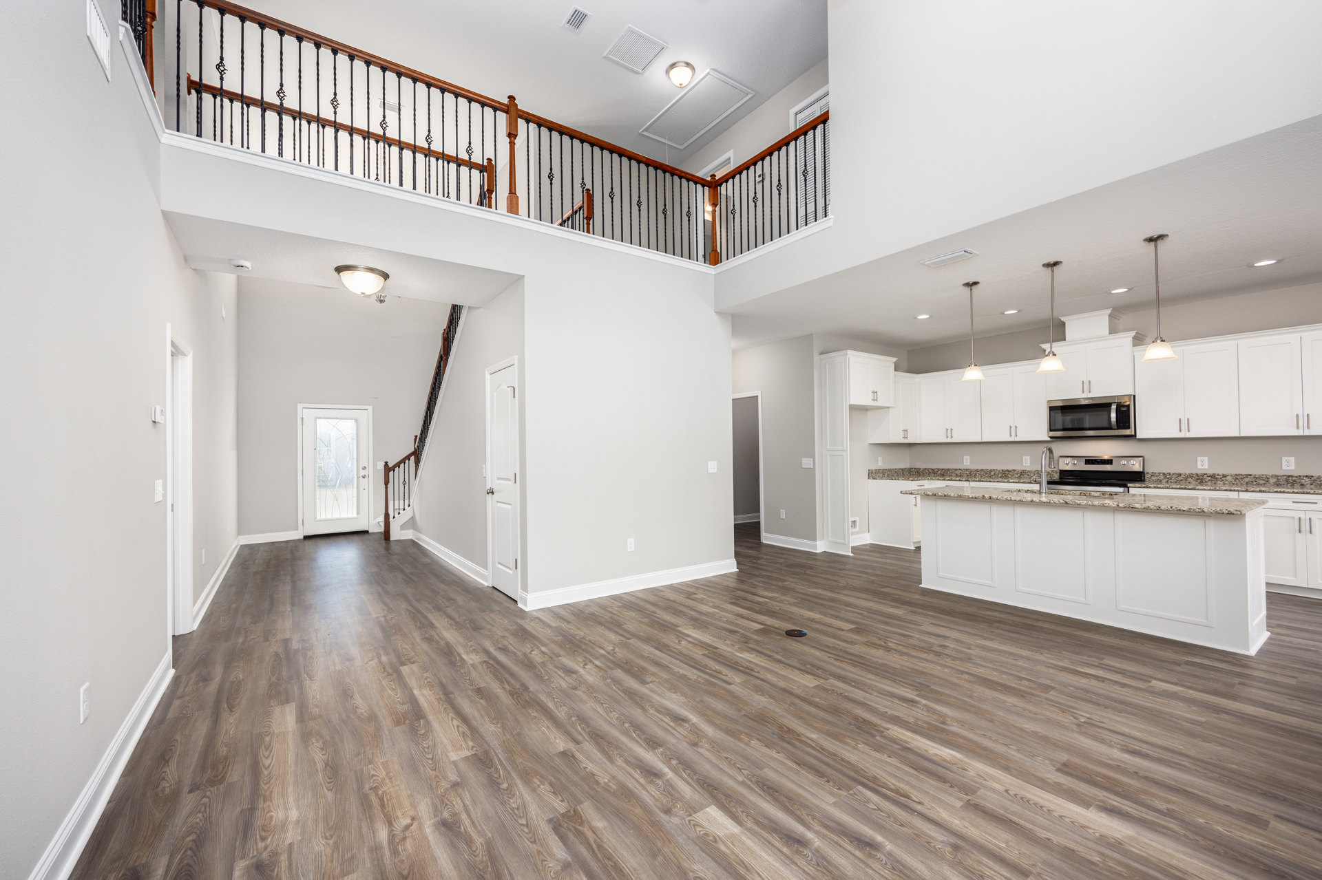 Open kitchen with wood flooring, white cabinetry, stainless steel microwave and oven, glass-paneled door, staircase leading to upper level, remote resting on floor
