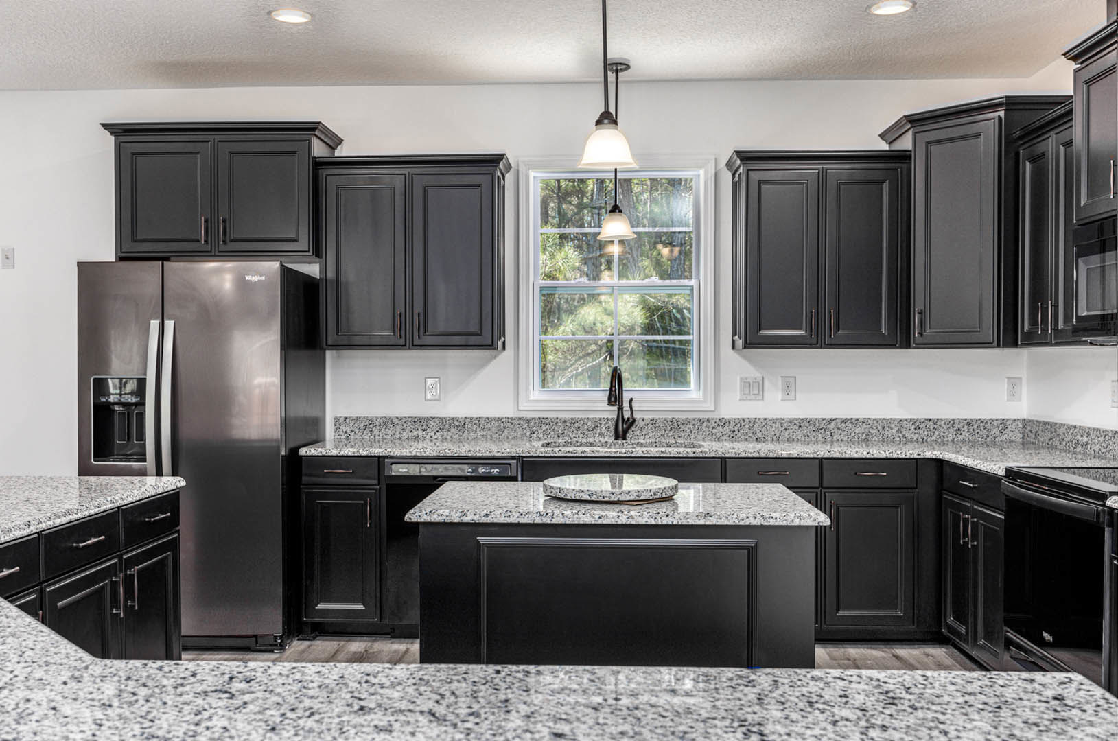 Granite countertops with undermount sink, stainless steel refrigerator, white cabinetry, pendant light fixture near window, round decorative object on counter, partial view of