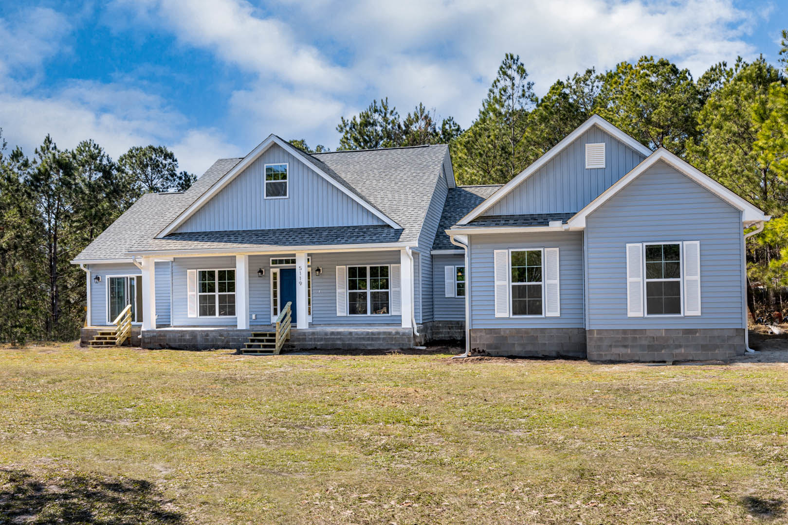 Two-story brick house with white shuttered windows, wooden porch stairs, and grassy yard bordered by mature trees