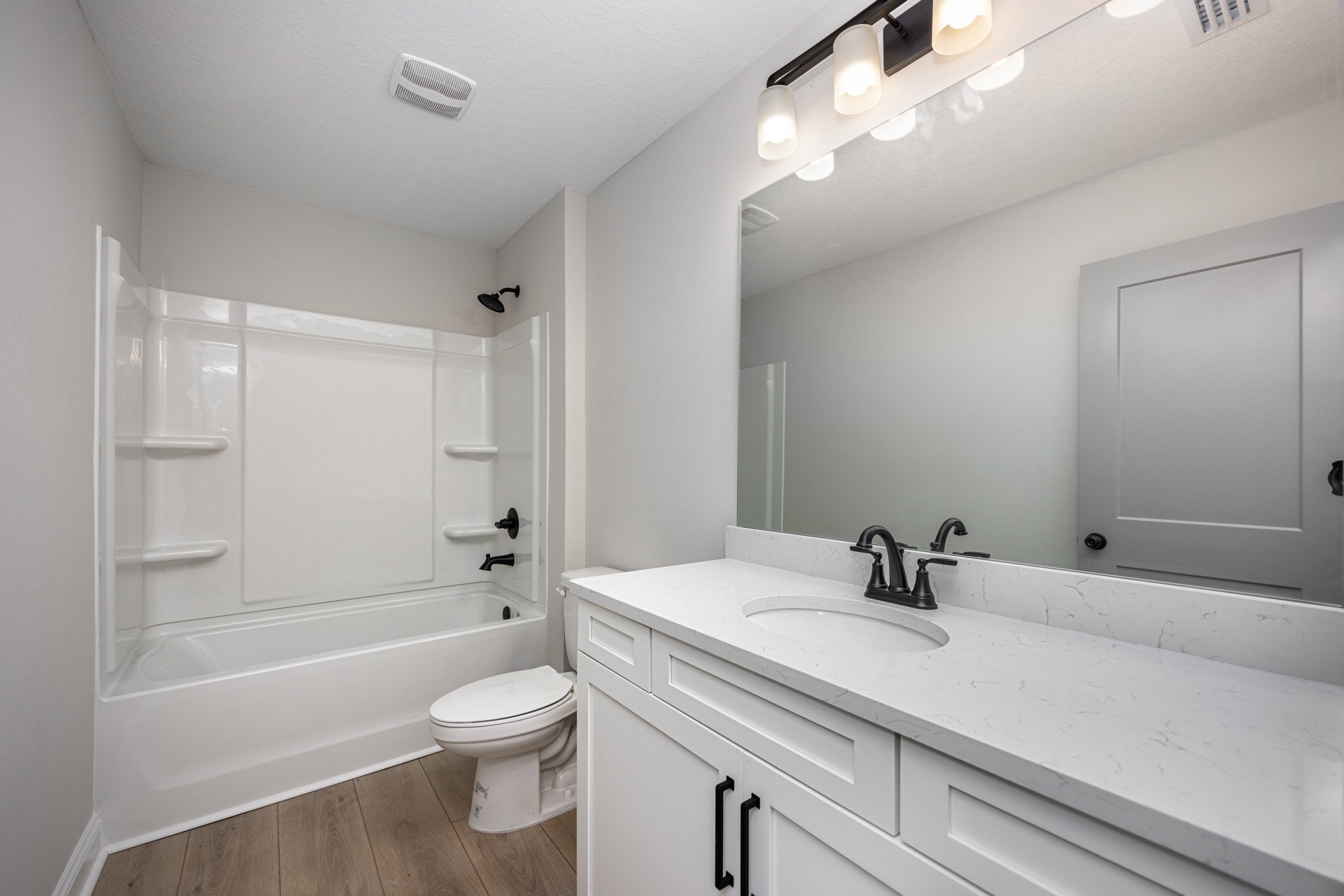White bathroom featuring a marble countertop with black faucet, rectangular sink, freestanding bathtub, closed toilet, white door with black handle, illuminated ceiling light, and