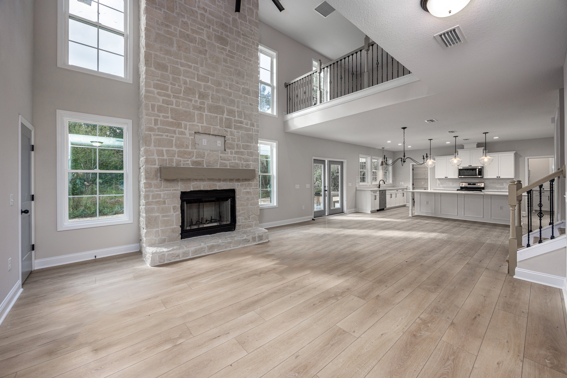 Spacious living room featuring wood flooring, black-framed fireplace, large windows overlooking forest, glass doors, and plaster walls.