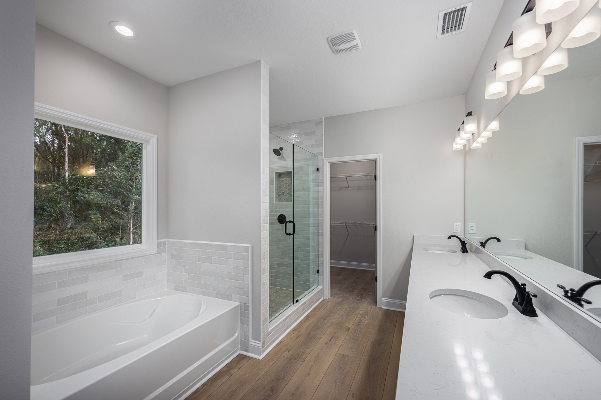 Bathroom featuring a white freestanding tub beside a tiled wall, glass-enclosed shower with matching tile, double vanity with sinks and chrome faucets, large window overlooking