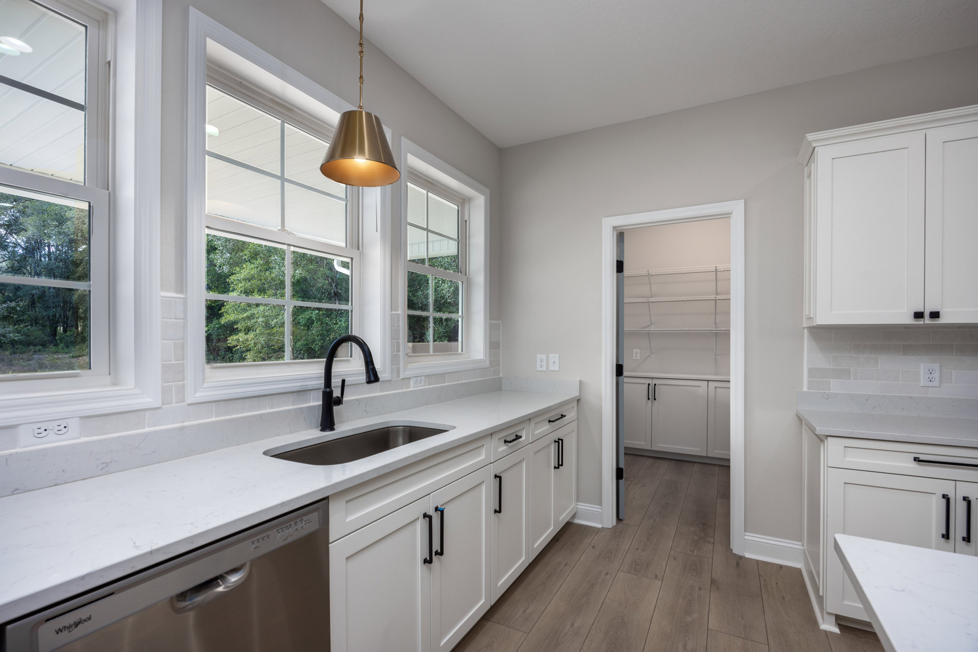 White shaker cabinets, quartz countertop, undermount sink with matte black faucet, gold pendant light, and stainless steel appliances in a modern kitchen.