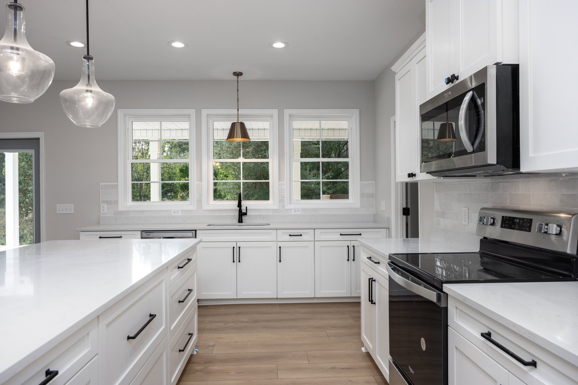 White kitchen with shaker cabinets, black appliances, black hardware, clear glass pendant light, and quartz countertops