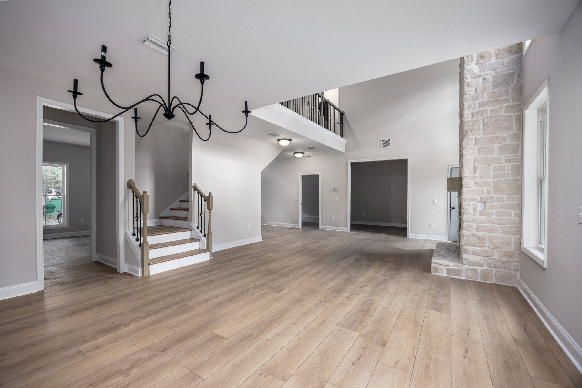 Spacious interior with hardwood floors, wood and metal staircase, open doorway, and modern chandelier hanging from plaster ceiling