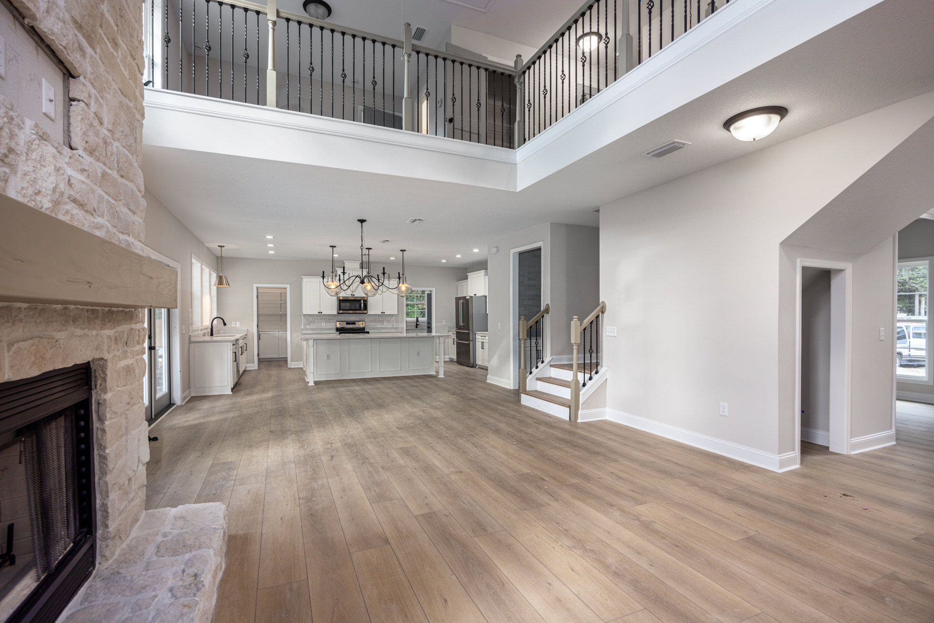 Open-concept room featuring wood flooring, a spacious kitchen with stainless steel appliances, white cabinetry, a refrigerator, built-in microwave and oven, a large staircase with