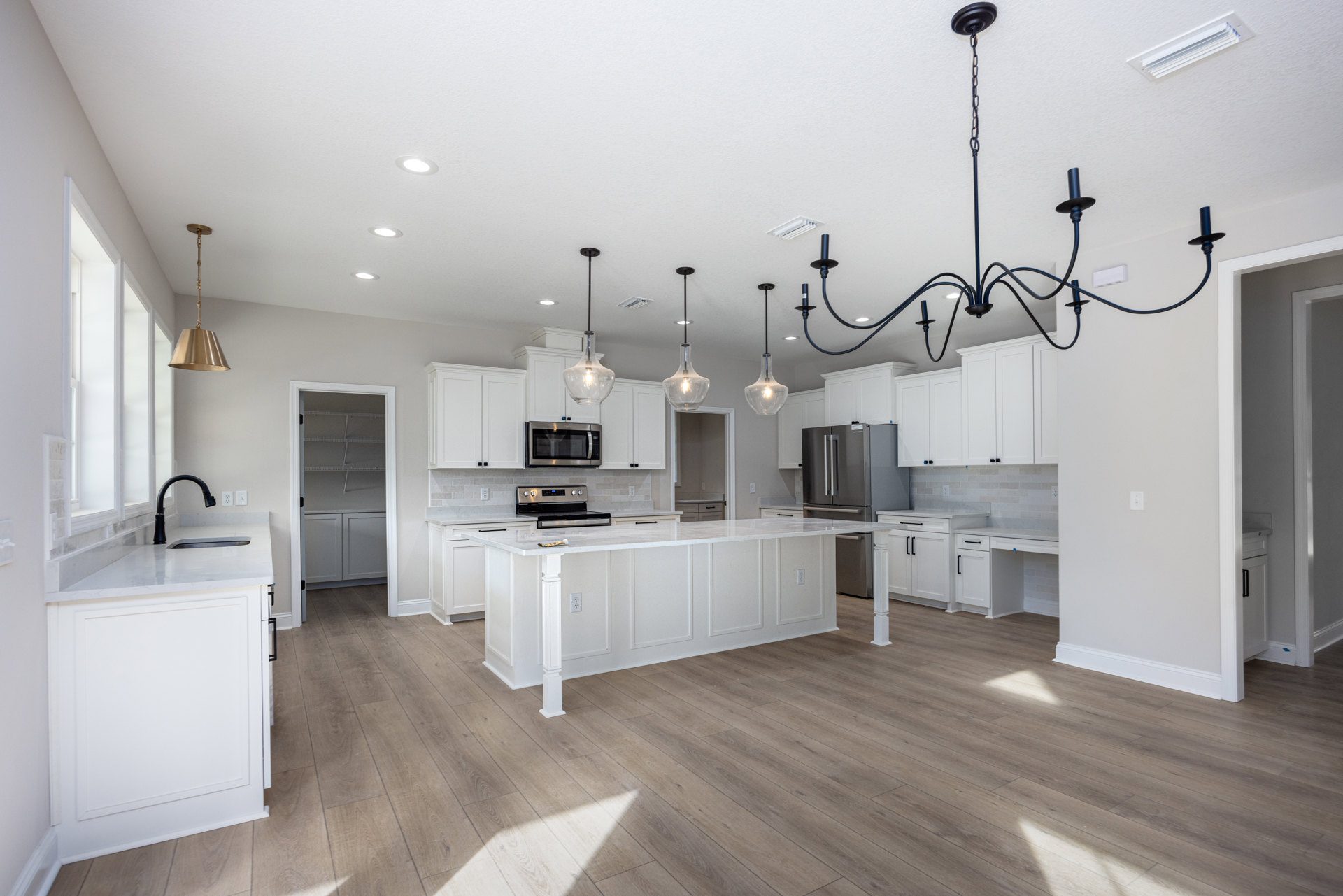 White kitchen with shaker cabinets, marble island countertop, stainless steel microwave, chandelier with exposed bulbs, wood flooring, and modern sink fixtures
