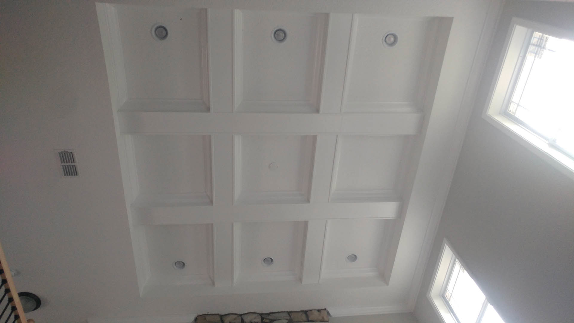 Recessed ceiling lights above textured stone accent wall, plaster ceiling molding, and window with natural light