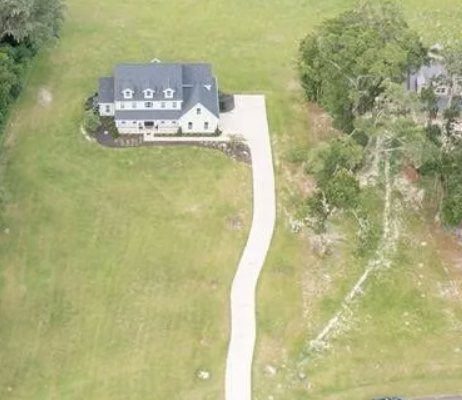 Modern two-story house with large windows, white exterior, and dark roof, set amid lush green grass and mature trees, stone pathway leading to entrance