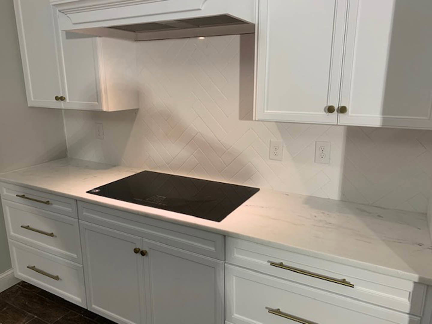 White kitchen with shaker cabinets, stainless stove, black countertop, white tile backsplash, white range hood, and visible drawer and outlet.