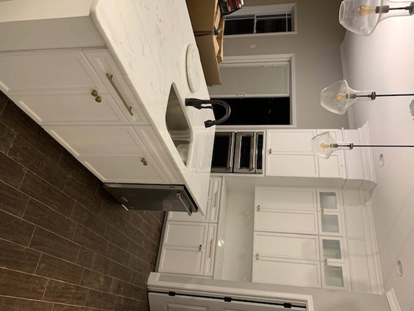 White shaker cabinets, stainless steel sink, light stone countertop, and neutral backsplash in a modern kitchen.