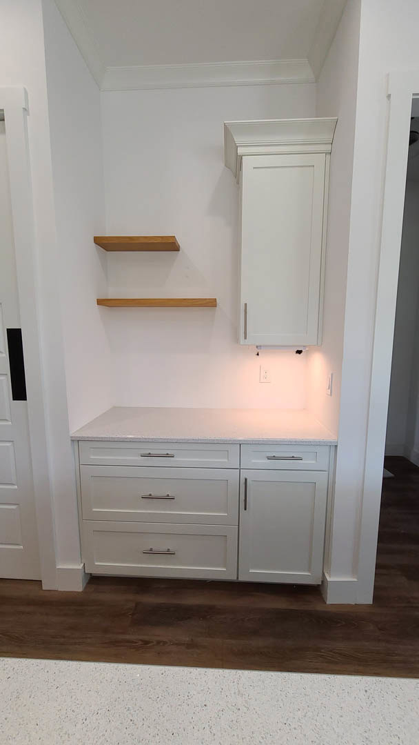 White kitchen with shaker cabinets and open shelves, silver drawer handles, white countertop, white door and frame, pink accent wall, brown wood flooring