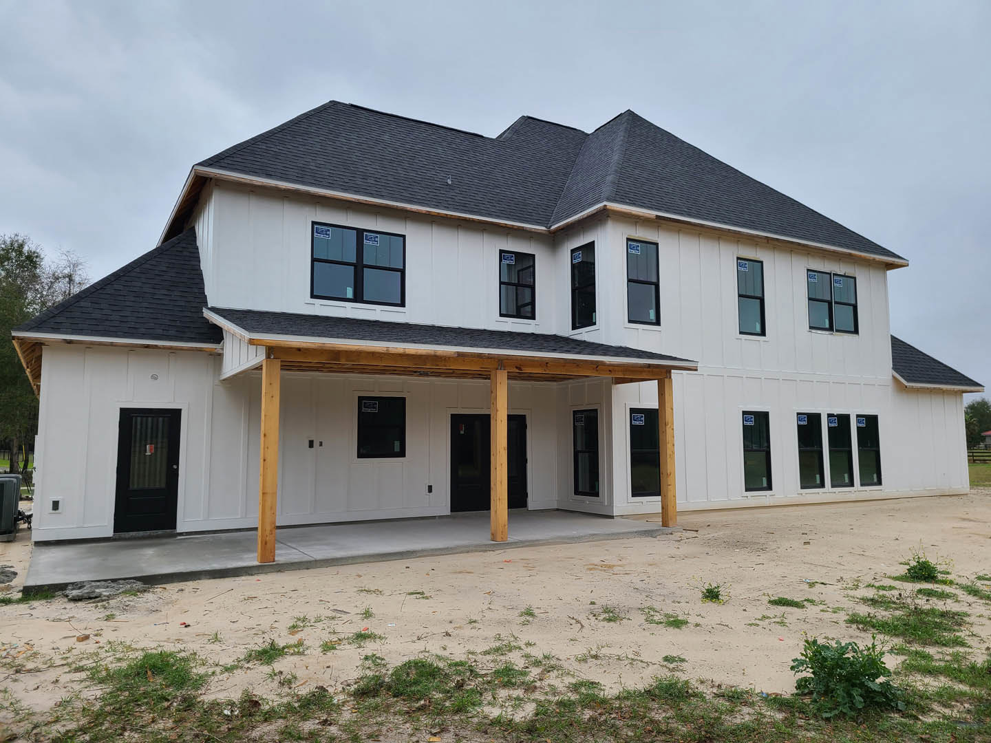 White two-story house with black roof, black-framed windows, wooden porch, black front door displaying a red and white sign, dirt patch in front yard.