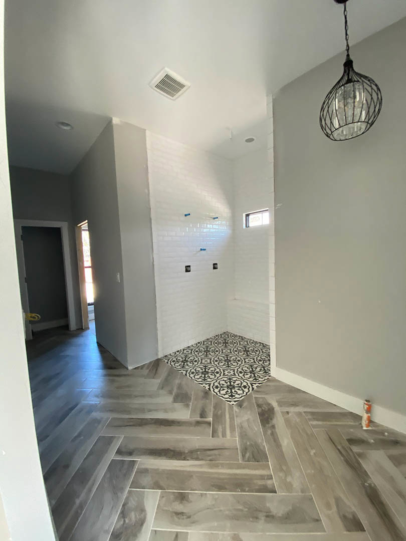 Open-concept room featuring transition between patterned black and white tile floor and warm wood flooring, white plaster walls, ceiling vent, recessed light fixture, and partial
