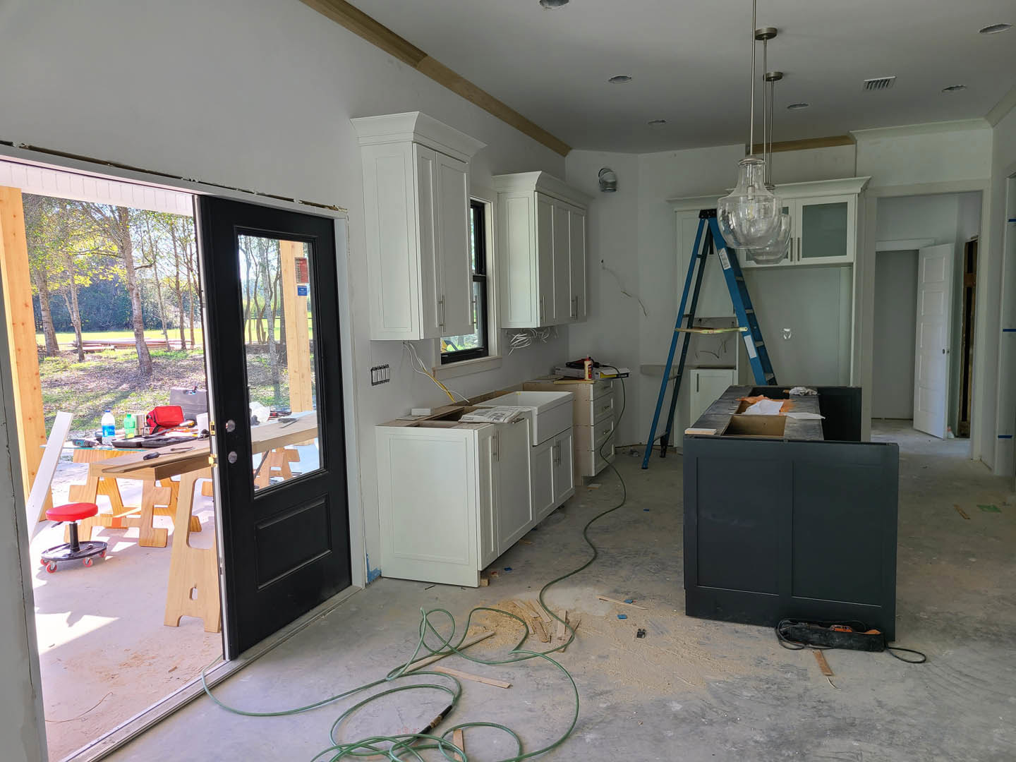 Kitchen with white shaker cabinets, built-in ladder on rail, light wood flooring, black desk and door, red rolling stool, white doors with black handles