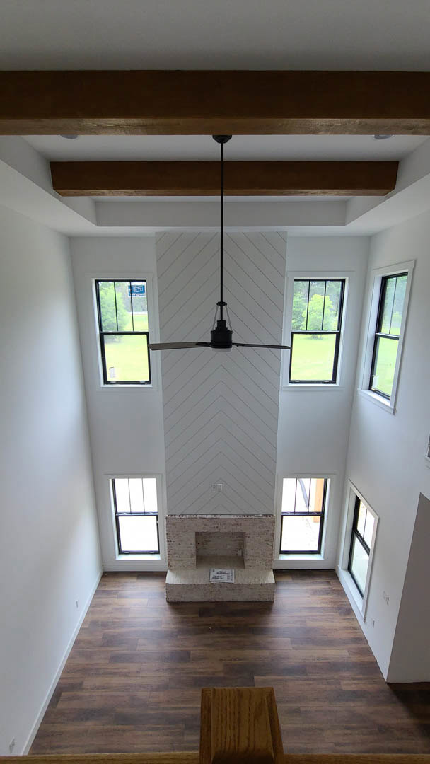Ceiling fan mounted on white ceiling above light wood flooring, white brick wall with square window framing green field outside