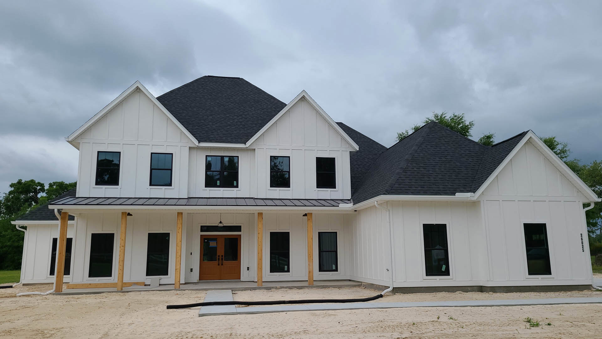 White siding house with black shingle roof, multiple large windows with black frames, double glass entry doors, tree visible through window, small sign posted on one window