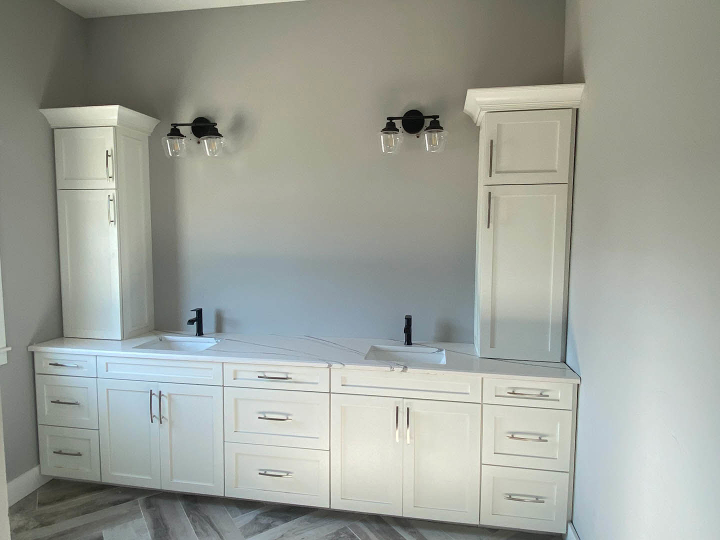 Bathroom with white cabinetry, dual sinks, silver hardware, and clear glass bulb light fixture; partial view of white refrigerator and close-up of drawer and cabinet handles.