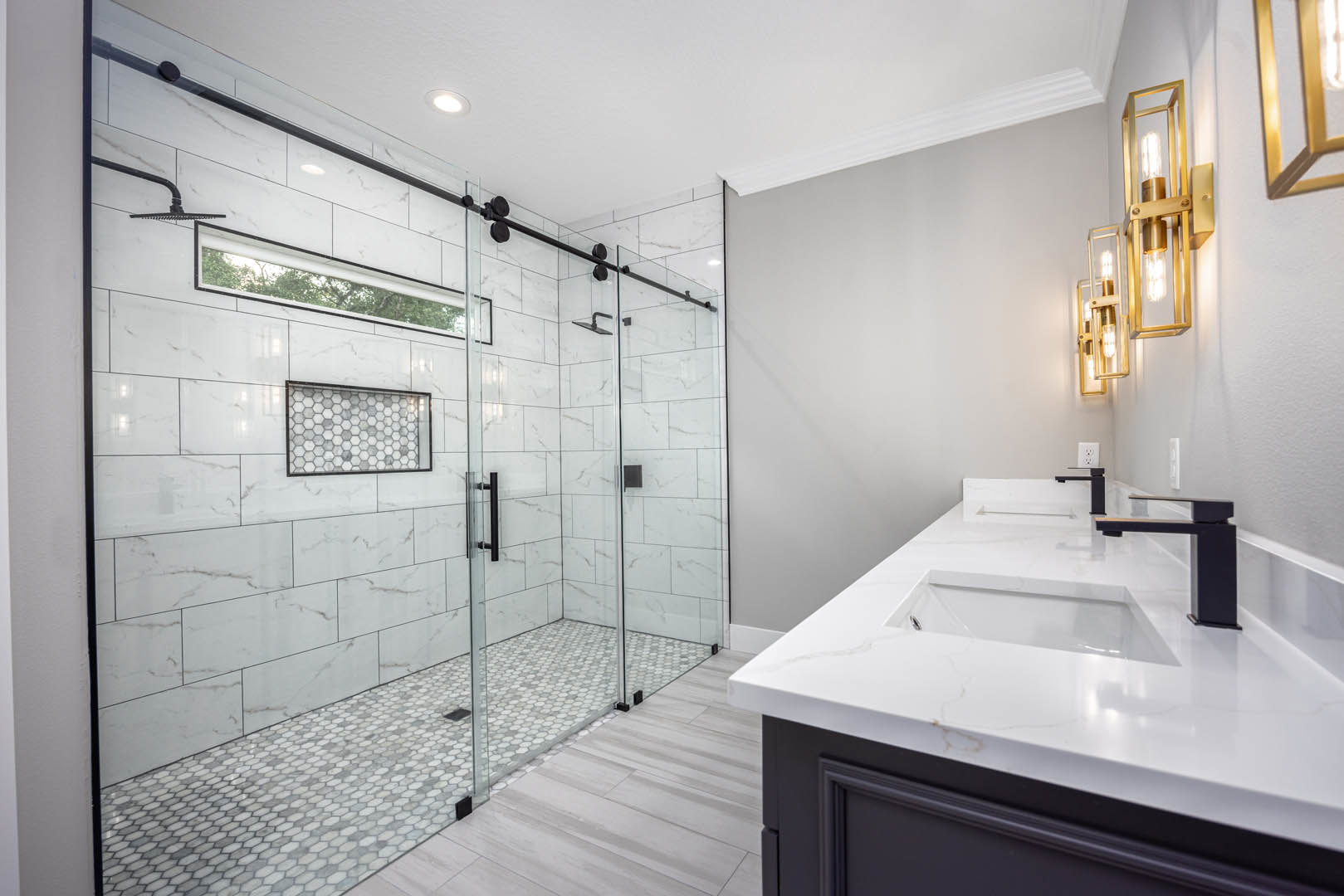 Bathroom featuring a glass shower enclosure, hexagonal tile accent wall, white countertop with integrated sink, gold faucet, and square drain opening.