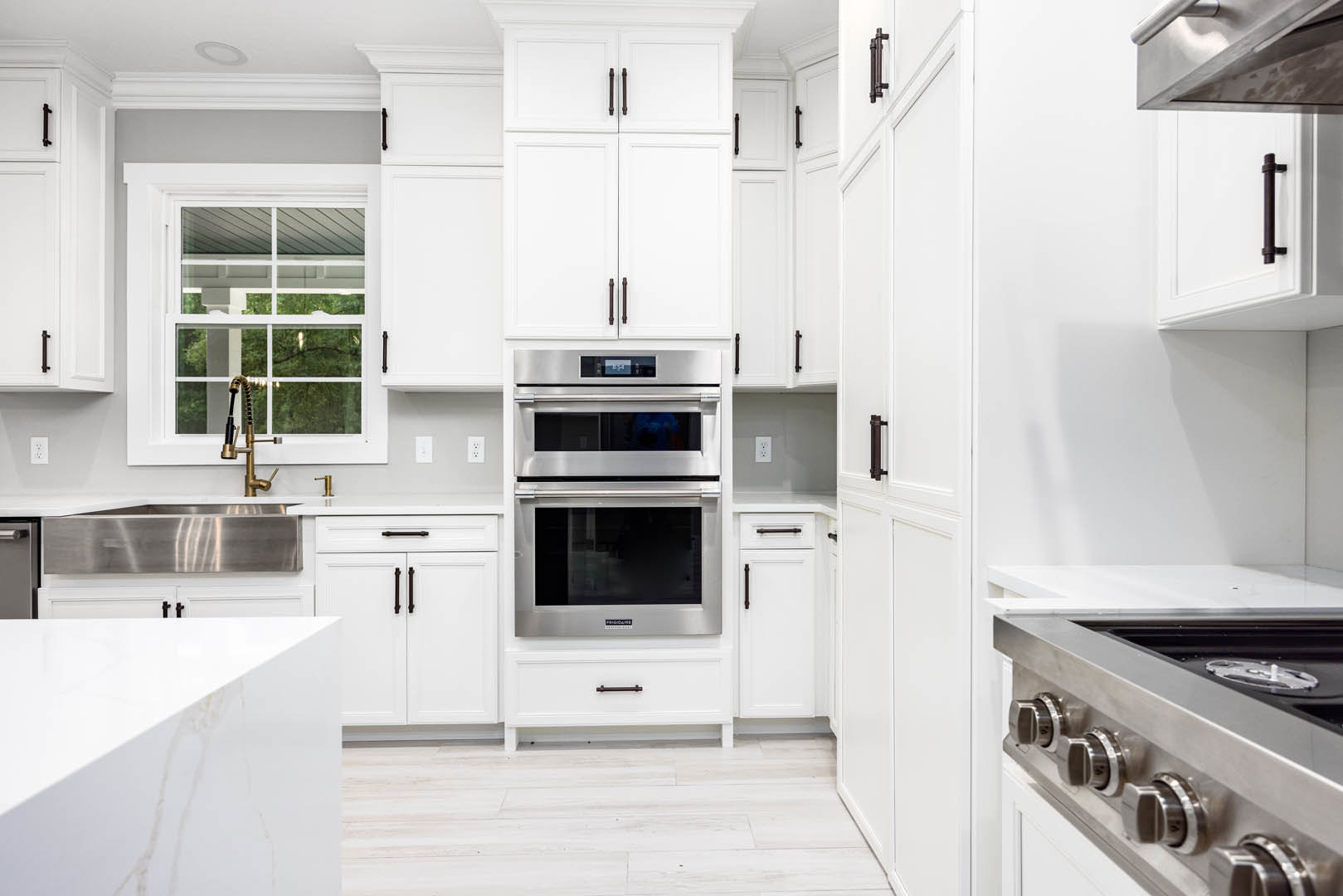 White shaker cabinets, stainless steel double oven, microwave, and stove, light quartz countertops, undermount sink, white tile backsplash