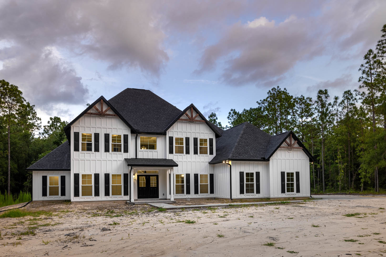 Large white house with black trim and shutters, surrounded by trees and clouds, dirt road with grass leading to the property, close-up of white-framed window