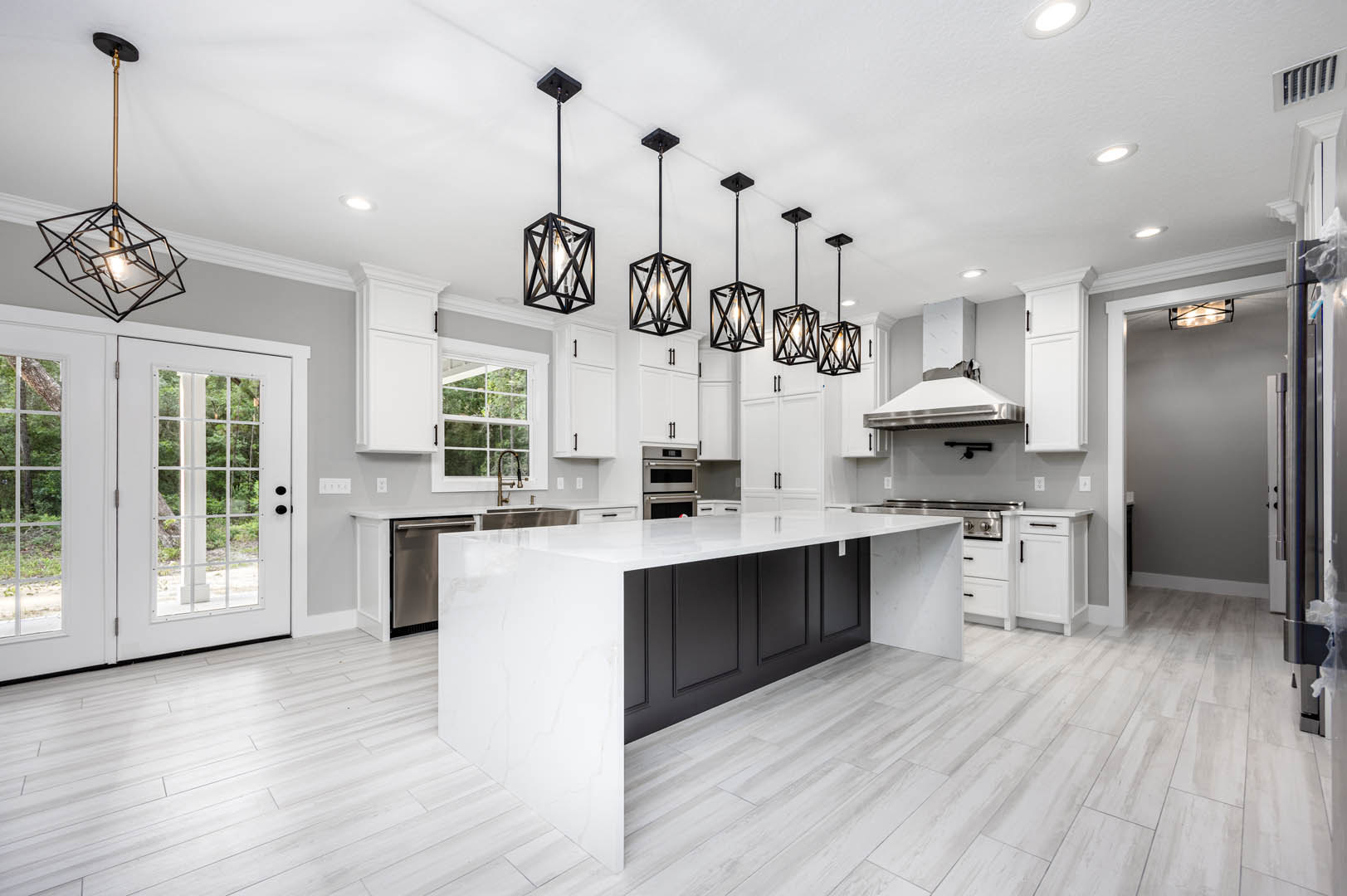 White kitchen with shaker cabinets, black appliances, quartz countertops, glass-paneled door, and modern chandelier hanging from the ceiling