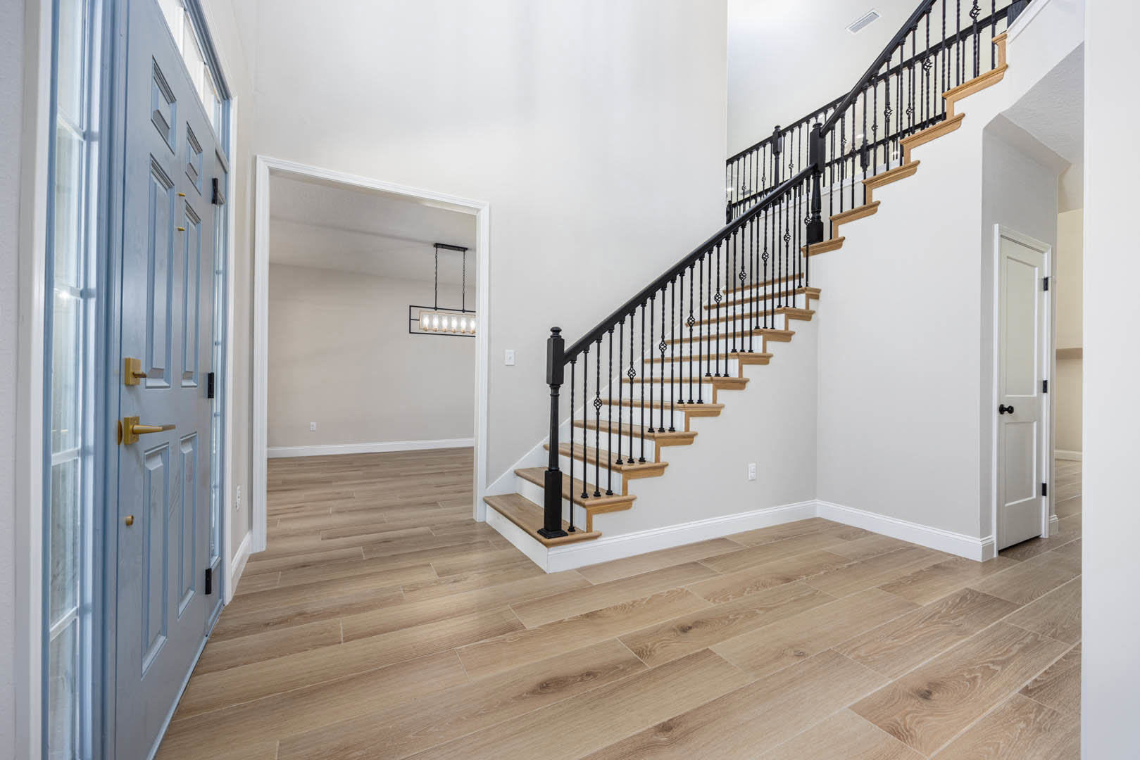 Wood staircase with black metal railings, white walls, laminate flooring, and a white door with black hardware
