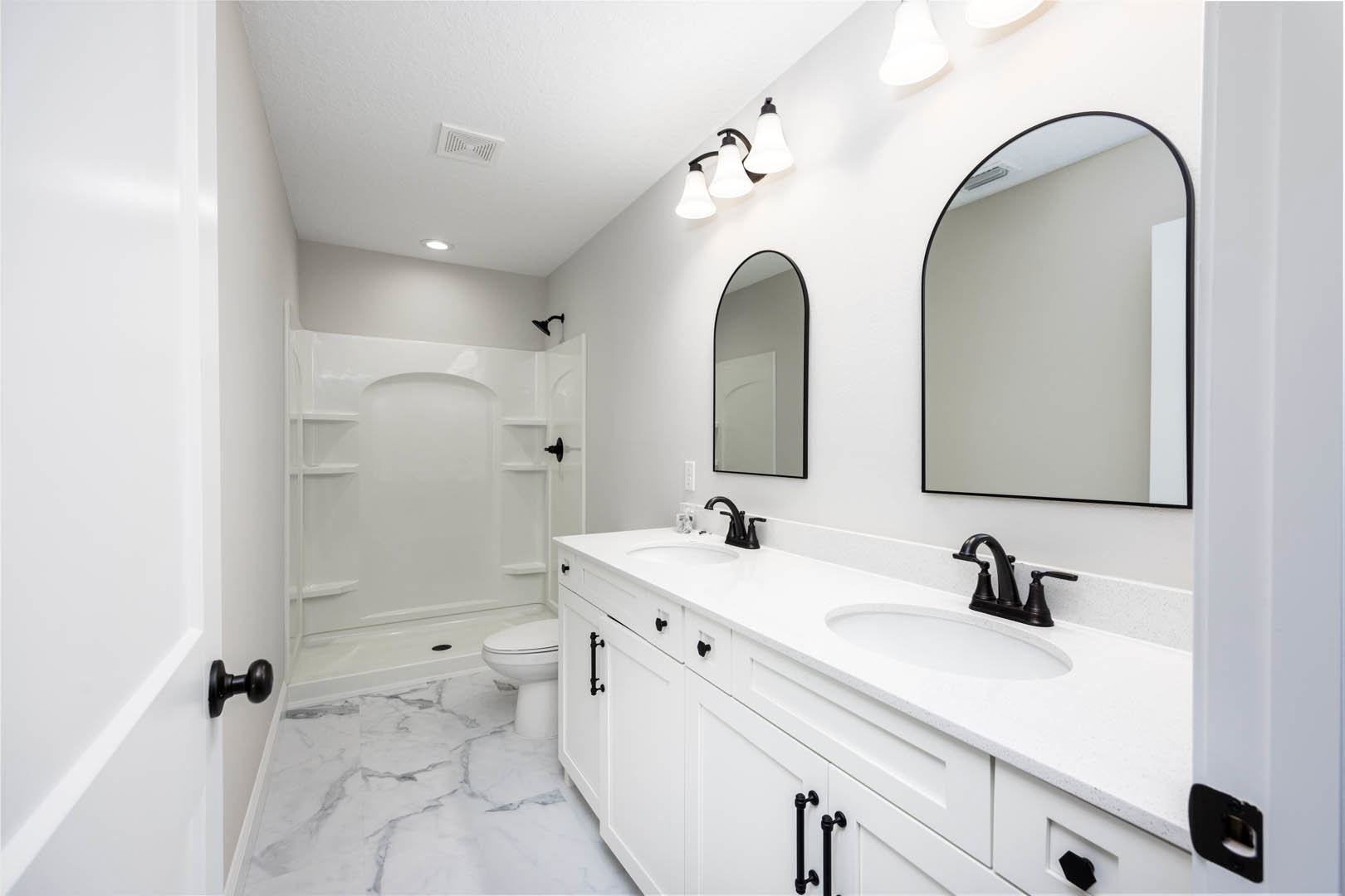 Bathroom featuring white cabinetry and countertops, black-framed mirror above sink, close-up of chrome faucet, white door with black border and black door knob, white shower with