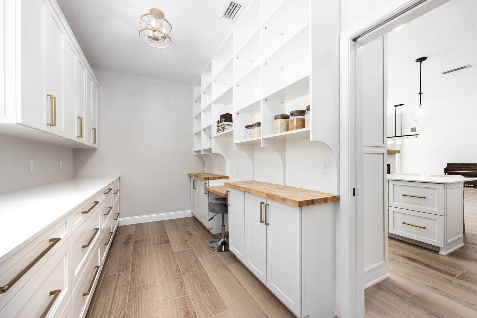 White kitchen with built-in shelves, shaker cabinets, wood flooring, and metal base accents; close-up details include a pendant light fixture, jar of cereal, and microphone resting