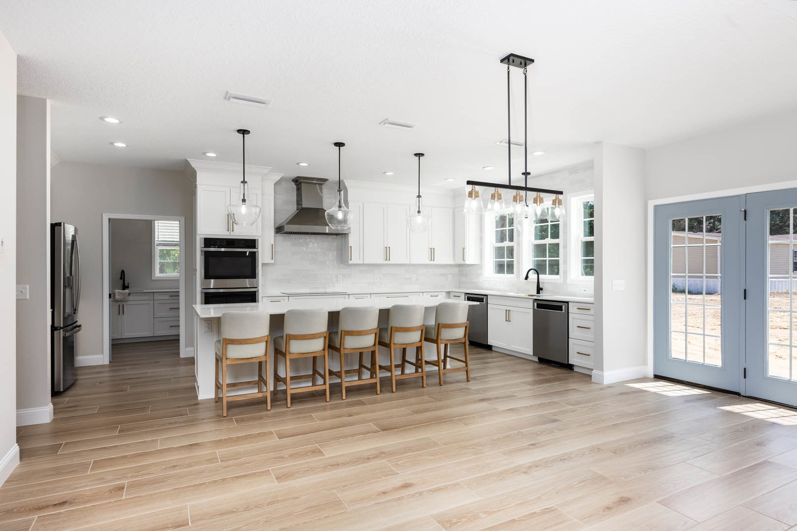 Spacious kitchen featuring a large central island with seating, expansive window, white cabinetry, stainless steel appliances including microwave and oven, wood flooring