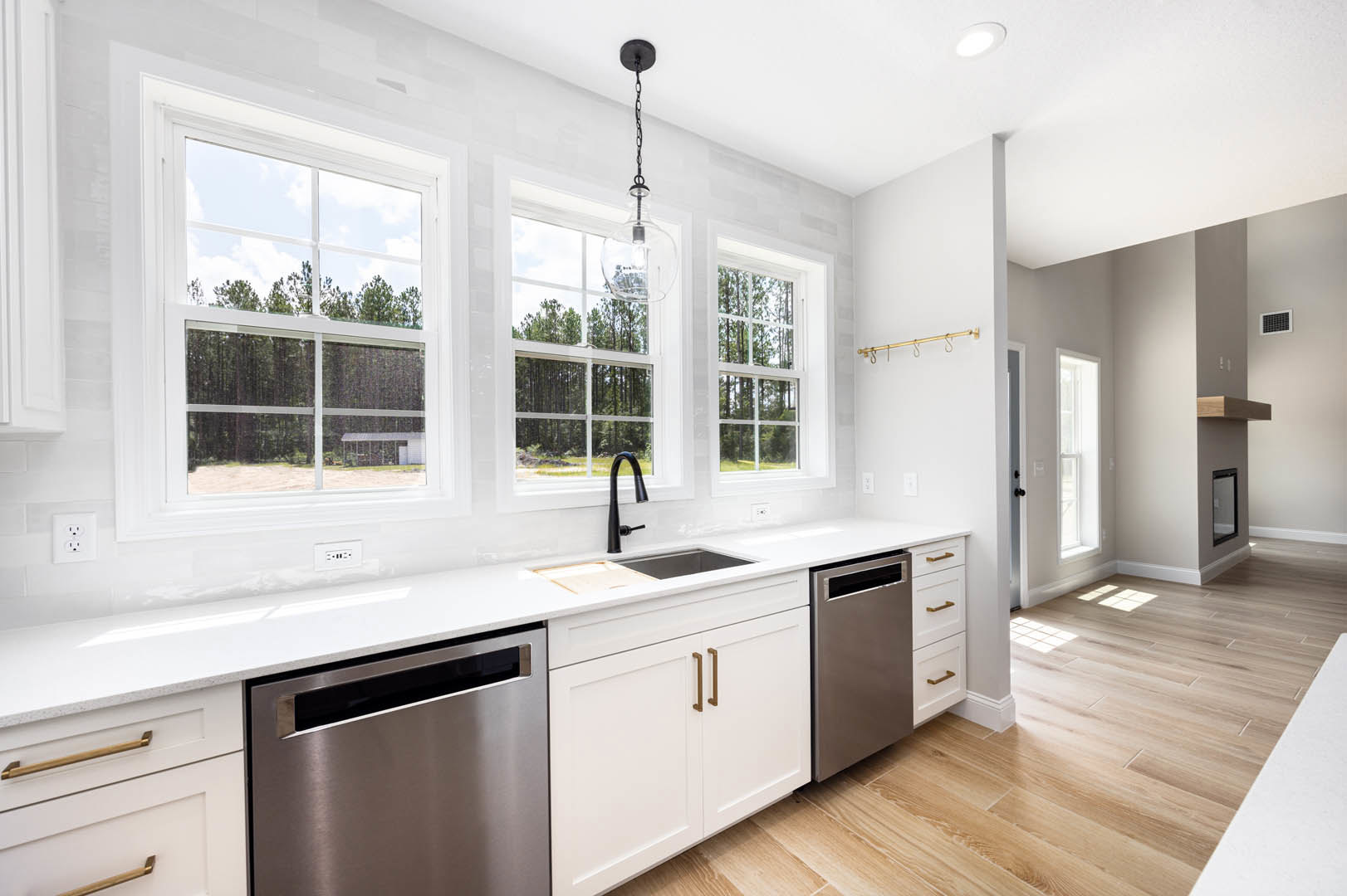 White kitchen with shaker cabinets, stainless steel appliances, grey countertop, pendant light fixture, window overlooking trees.