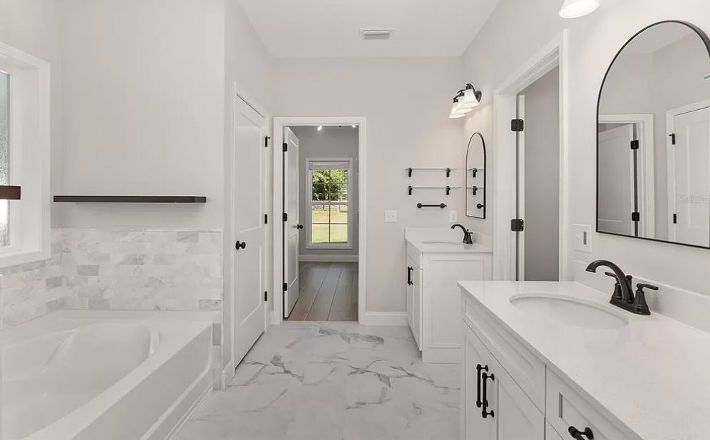 Bathroom featuring polished marble floor, white painted walls, freestanding bathtub, chrome fixtures, and modern sink with tile accents
